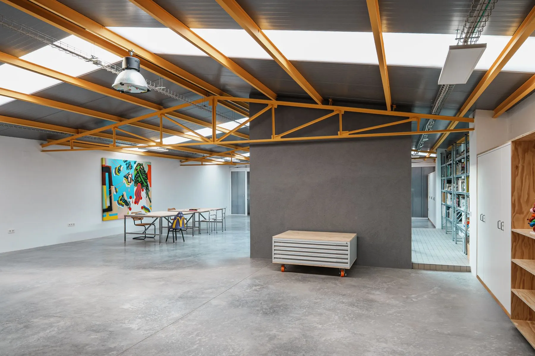 Espacio Níquel: sala principal con vigas amarillas, un cuadro de colores y mesas de trabajo